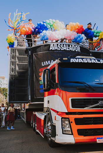 Foto do Trio Elétrico na 7ª Marcha pela Diversidade de Curitiba, em 2024. Ele está decorado com balões e há algumas pessoas em cima que podemos ver na foto.
